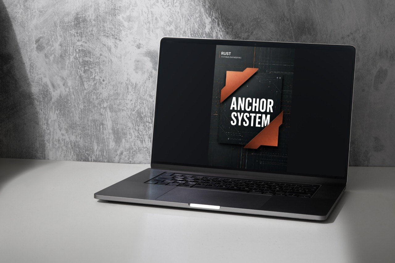 A dark gray laptop sits open on a white surface against a textured gray wall, displaying a software cover for 'Anchor System' on its screen.